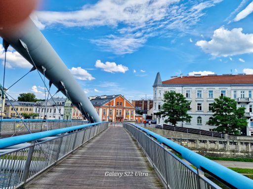 Krakau Holzbrücke mit blauen Geländern, umgeben von Gebäuden und Himmel mit Wolken.