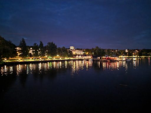 in Schweden am Vänernsee Eine ruhige Flusslandschaft bei Nacht mit beleuchteten Ufern und spiegelndem Wasser.