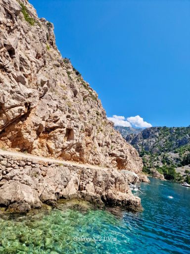 Kroatien Insel Rab Klarer blauer Himmel über einer felsigen Küstenlandschaft mit türkisfarbenem Wasser.